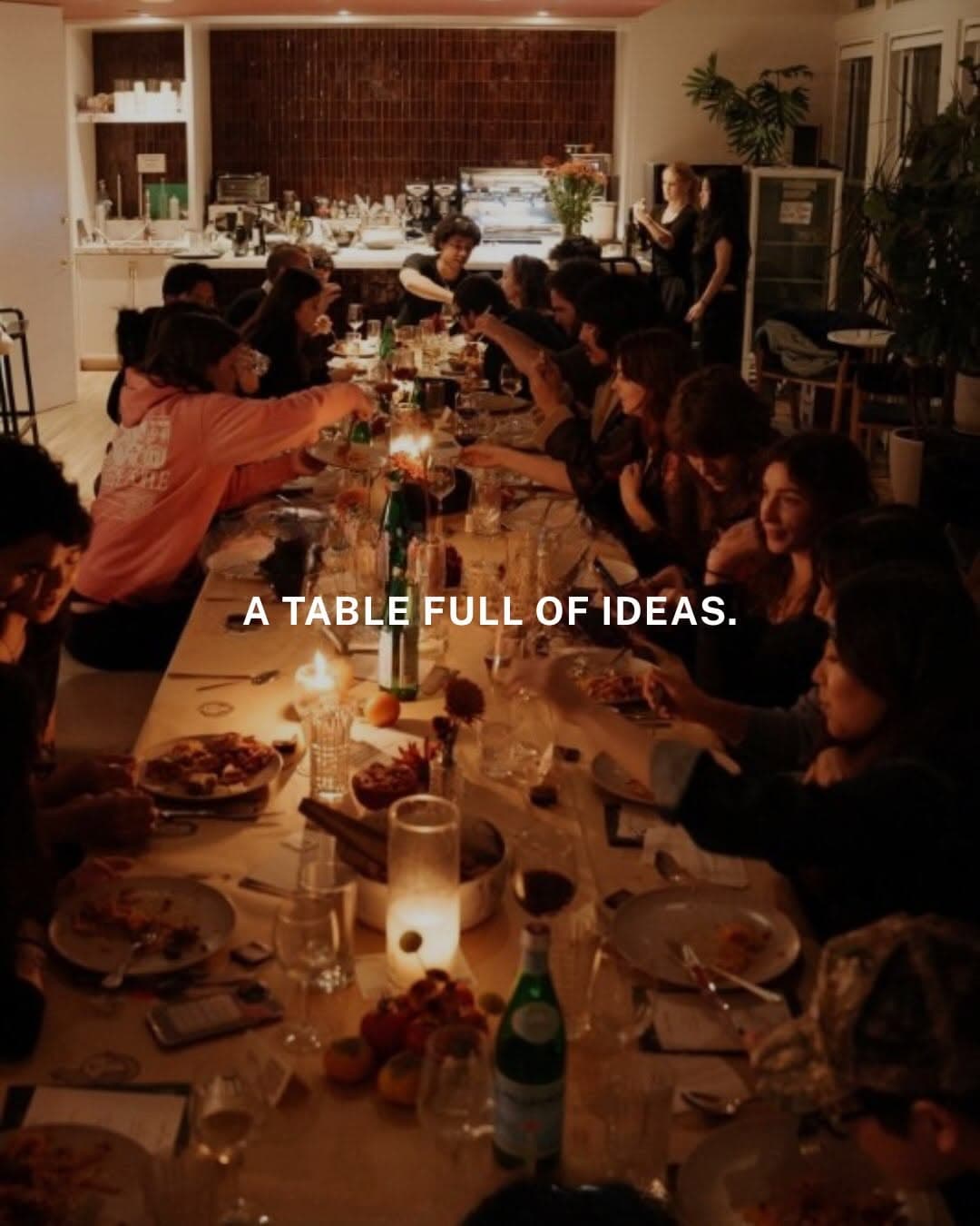 A long communal dinner table in New York set for 20 creatives, with shared plates and guests in conversation.